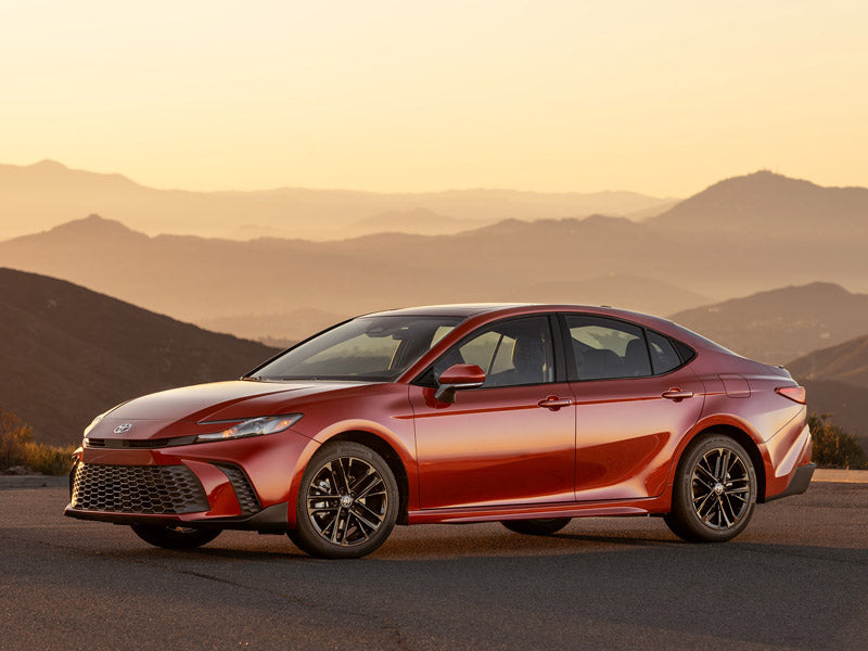 Red sedan car parked with mountains in the background.