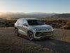 Gray SUV parked on dirt road with mountains in the background.