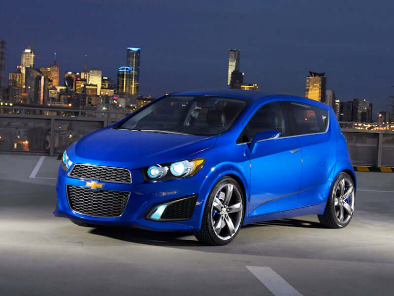 Blue Chevrolet hatchback car in front of a city skyline at night.