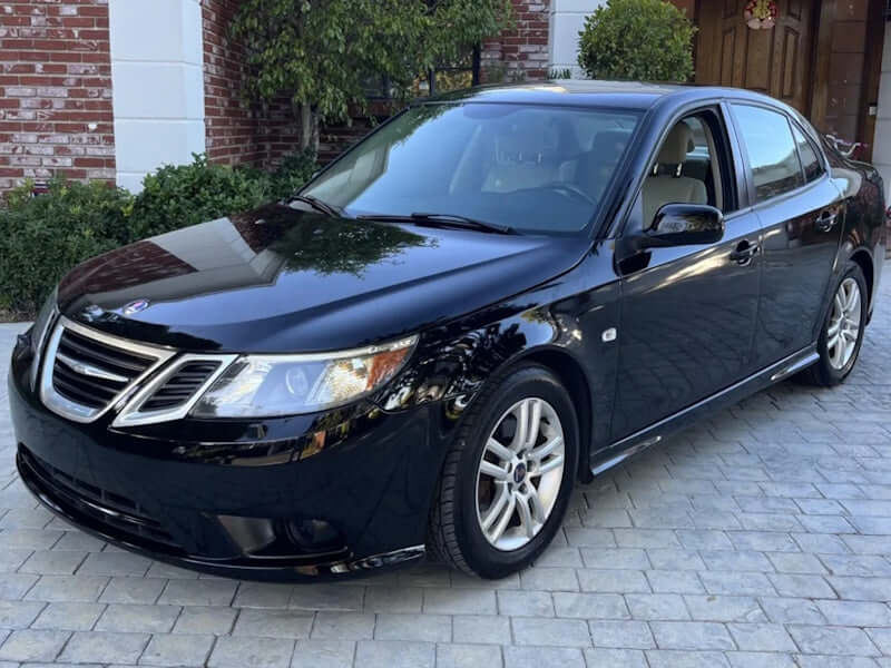 Black Saab sedan parked on brick pavers.